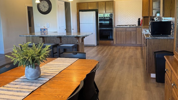 A modern kitchen with wooden cabinets, a built-in oven, and a dining area with a wooden table and chairs.