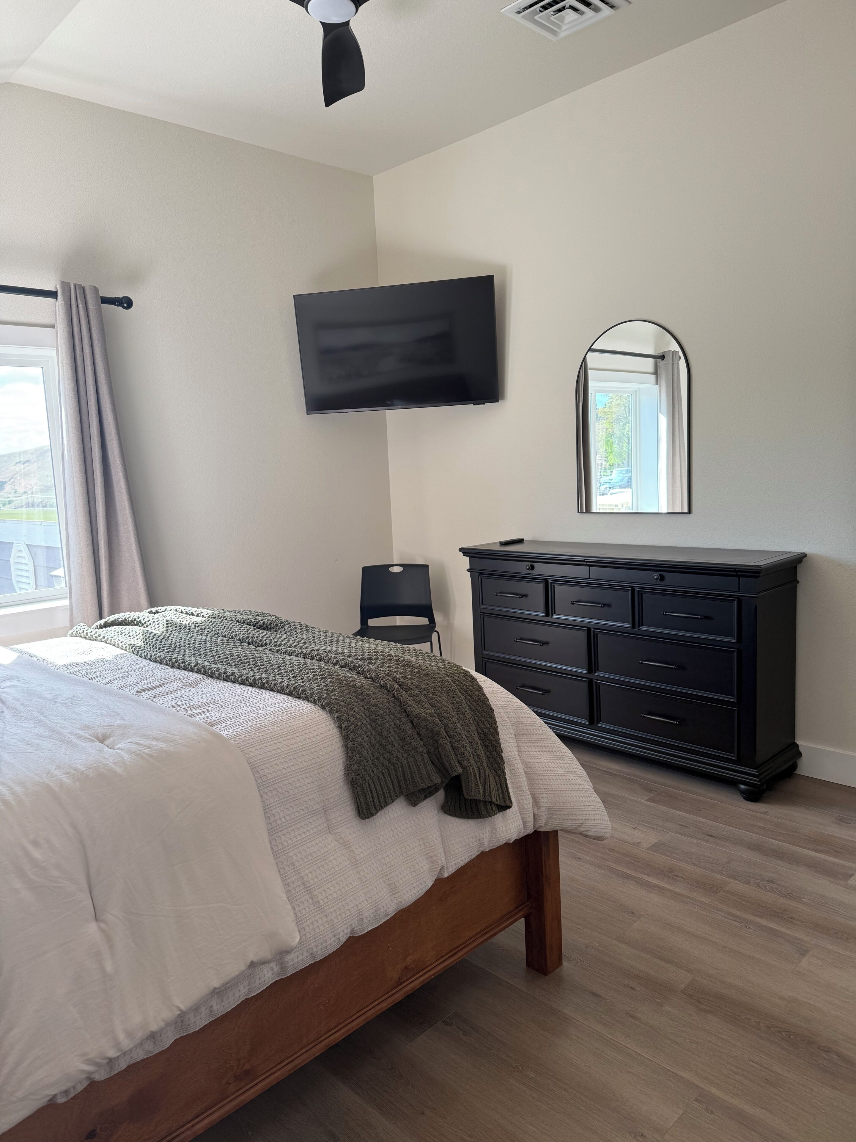 Een slaapkamer met een bed, een dressoir, een televisie en een spiegel.