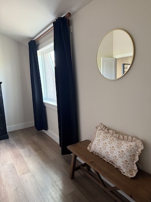 A room with a wooden bench, a round mirror, and a window with dark curtains.