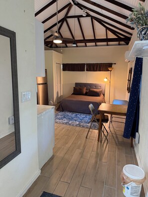 Habitació petita amb un llit, taula, cadira, escriptori, làmpada i ventilador de sostre.