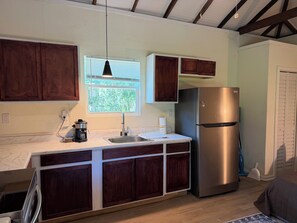 A kitchen with a stainless steel refrigerator, wooden cabinets, a marble countertop, and a window with blinds. - Sleep well in our charming cottage in Eustis with cool AC. (Eustis)