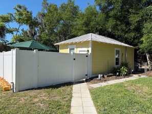 A yellow house with a white fence, a green umbrella, and a paved pathway. - Sleep well in our charming cottage in Eustis with cool AC. (Eustis)