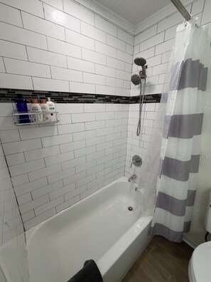 Een badkamer met witte betegelde wanden, een bad, een douche en een toilet.