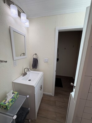 A bathroom with a white sink, mirror, and towel ring. There is a green tissue box on a shelf. - Sleep well in our charming cottage in Eustis with cool AC. (Eustis)
