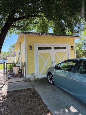 A yellow building with a white garage door, a parked car, and a tree in the background.