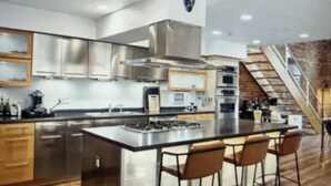 A modern kitchen with a central island, bar stools, and a staircase leading to an upper level.