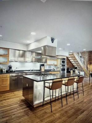 A modern kitchen with a central island, bar stools, and a staircase leading to an upper level.