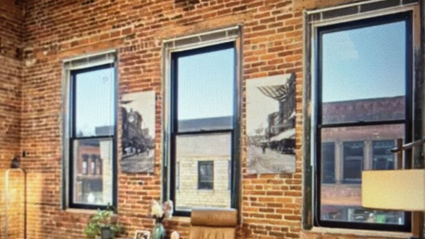 A room with a brick wall, large windows, a sofa, a coffee table, and a chair.