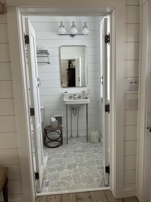 Un baño con piso de piedra, un lavamanos blanco, un espejo y un perchero para toallas.