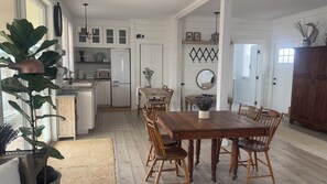 Una cocina con armarios blancos, un refrigerador, una mesa de comedor con sillas y una planta grande en maceta.