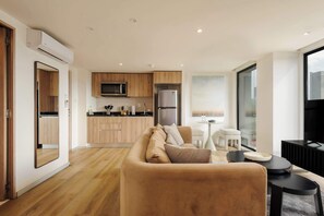 Ein modernes Wohnzimmer mit einer Couch, einem Esstisch und einer Küchenzeile mit Holzschränken und Geräten.