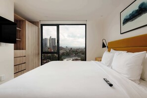 Ein Hotelzimmer mit Bett, Blick auf die Stadt, einem an der Wand montierten Fernseher und einem Holzschrank.