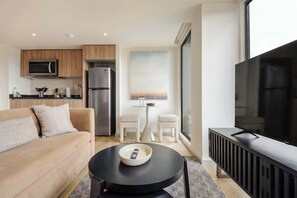 Ein modernes Wohnzimmer mit einer Couch, einem Esstisch mit zwei Stühlen, einem Fernseher und einer Küchenzeile mit Mikrowelle, Kühlschrank und Schränken.