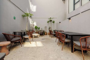 Ein Café mit Tischen, Stühlen, Topfpflanzen und einem grünen Ausgangsschild.