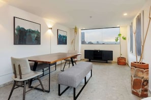 Ein moderner Essbereich mit einem Holztisch, einer Bank und Blick auf die Stadt durch große Fenster.