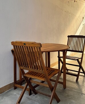 A wooden table and two chairs in a room with a plain wall and a concrete floor. - Vrbo Property (Staranzano)