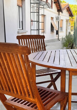 A wooden table and chairs outside a building with a white exterior and brown shutters. - Vrbo Property (Staranzano)