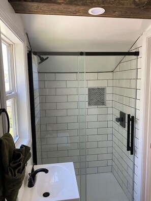 A bathroom with a glass shower enclosure, white tiled walls, a white sink, and a towel rack. - Tranquil studio with AC in charming Pulaski perfect for getaway (Pulaski)