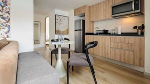 Une cuisine moderne équipée d’un four à micro-ondes, d’un réfrigérateur et de meubles de rangement en bois. Un coin repas avec une table et des chaises est également disponible.
