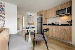 Eine moderne Küche mit Mikrowelle, Kühlschrank und Holzschränken. Es gibt einen Essbereich mit Tisch und Stühlen.
