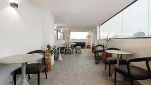 Un intérieur moderne comprenant un coin repas, des chaises, des tables, des plantes en pot et une grande fenêtre donnant sur la ville.
