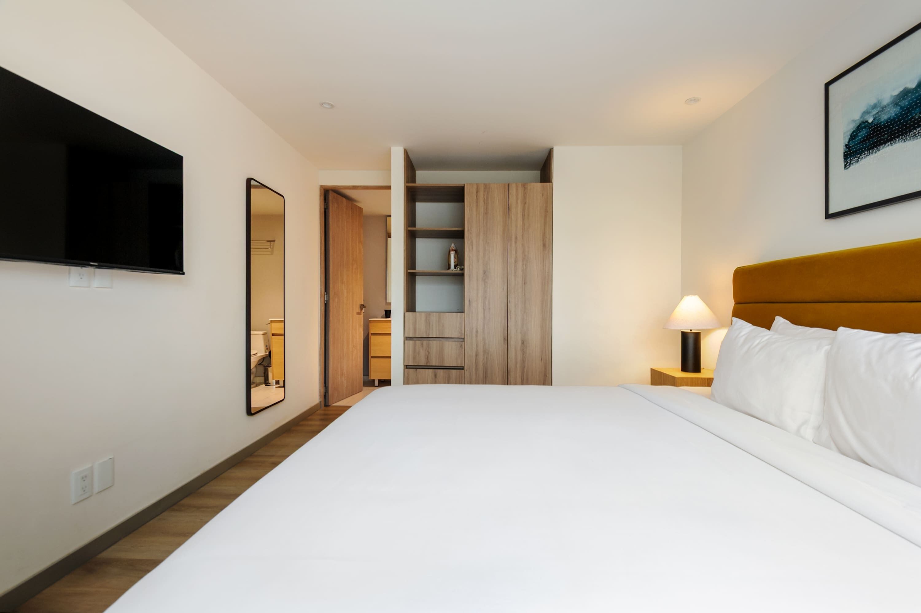 A hotel room with a bed, a TV, a mirror, a wardrobe, and a nightstand with a lamp.