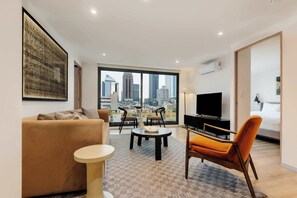 A modern living room with a sofa, a coffee table, and a TV. There is a large window with a city view. - w* | Stunning 2BR in Cuauhtemoc (Ciudad de México)