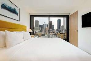 A hotel room with a large bed, a yellow headboard, white bedding, a city view through floor-to-ceiling windows, and a mounted television on the wall. - w* | Stunning 2BR in Cuauhtemoc (Ciudad de México)