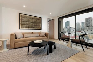A modern living room with a sofa, two tables, and chairs, a large window with a city view, and a framed artwork on the wall. - w* | Stunning 2BR in Cuauhtemoc (Ciudad de México)