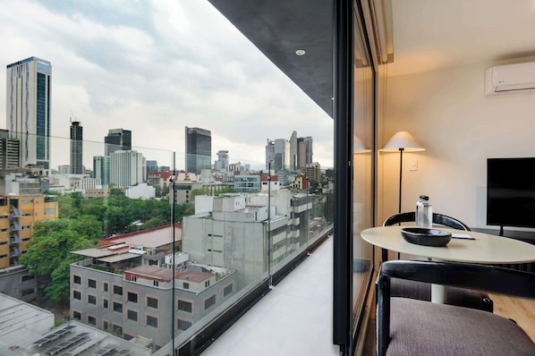 Ein modernes Hotelzimmer mit Blick auf die Stadt, ein runder Tisch mit einer Schüssel und einer Flasche sowie ein Flachbildfernseher an der Wand.