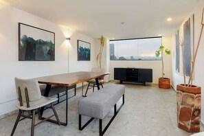 Ein moderner Essbereich mit einem Holztisch, einer Bank und Blick auf die Stadt durch große Fenster.
