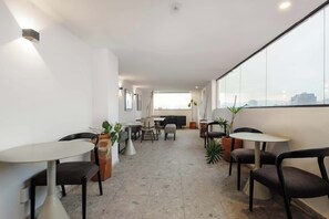 Ein modernes Interieur mit Essbereich, Stühlen, Tischen, Blumentöpfen und einem großen Fenster mit Blick auf die Stadt.