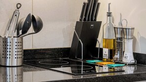 Eine Küchenarbeitsplatte mit einem Messerblock, einer Olivenölflasche, einem Salzstreuer, einer Pfeffermühle und einem Messbecher.