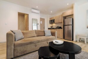 A modern living room with a sofa, a coffee table, a kitchen area with a refrigerator and microwave, and wooden cabinets. - w* | Bright 2BR in Cuauhtemoc w/ AC (Ciudad de México)
