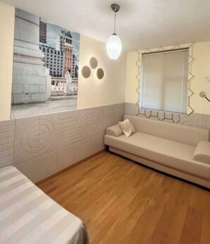 Habitació amb llit, sofà, llum penjada a la paret i finestra amb persianes.