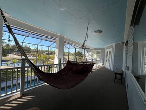 Eine Veranda mit einer Hängematte, Blick auf ein Gewässer und einem klaren Himmel.