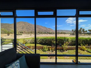 Ein Zimmer mit großen Fenstern und Blick auf einen angelegten Garten sowie entfernte Berge.