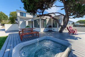 Ein modernes Haus mit Whirlpool, einer Holzterrasse und Sitzgelegenheiten im Freien.