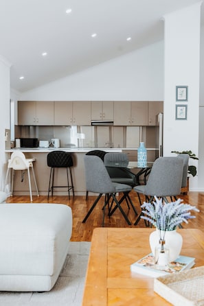 A modern kitchen with a dining area, a white sofa, and a coffee table with a vase.