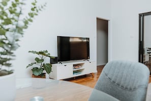 A modern living room with a flat-screen TV on a white cabinet, a grey sofa, and a potted plant.