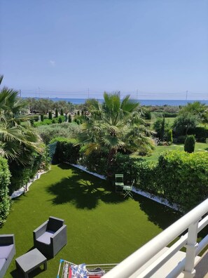 Un balcón con vista a un jardín cuidado y al mar.