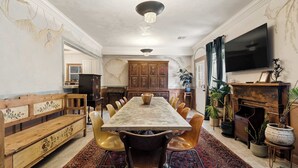 Un comedor con una mesa larga, sillas, un banco, un televisor y una chimenea.