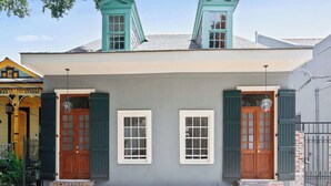 Una casa de dos pisos con un porche delantero, dos ventanas con contraventanas y una pequeña entrada de ladrillo.