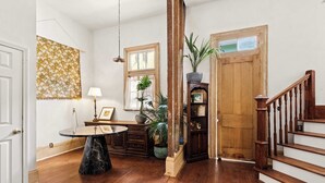 Una escalera de madera, una mesa redonda sobre base de mármol y un mueble de madera con una planta.