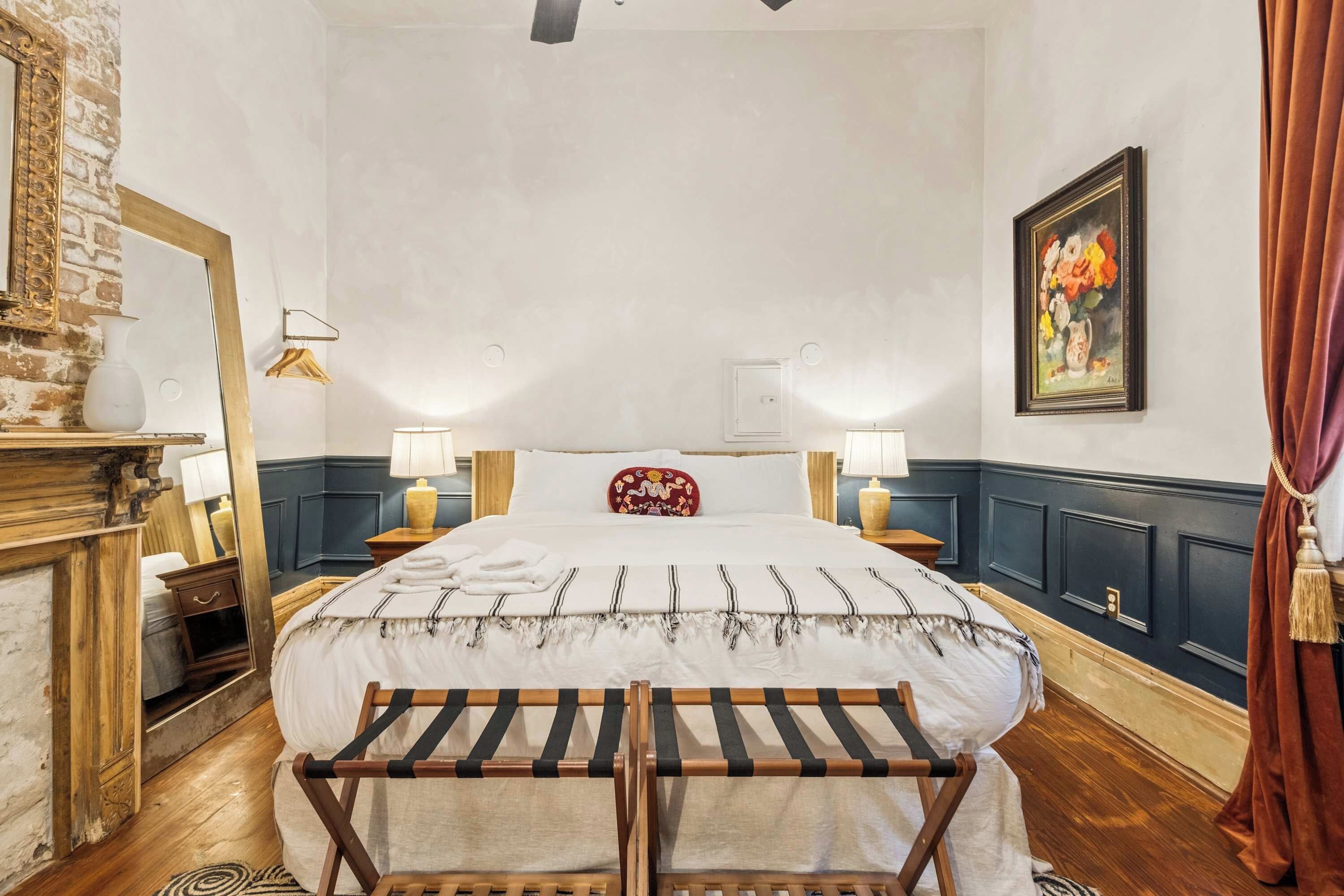 A hotel room with a large bed, two bedside tables, a wooden bench, a fireplace, and a painting on the wall.