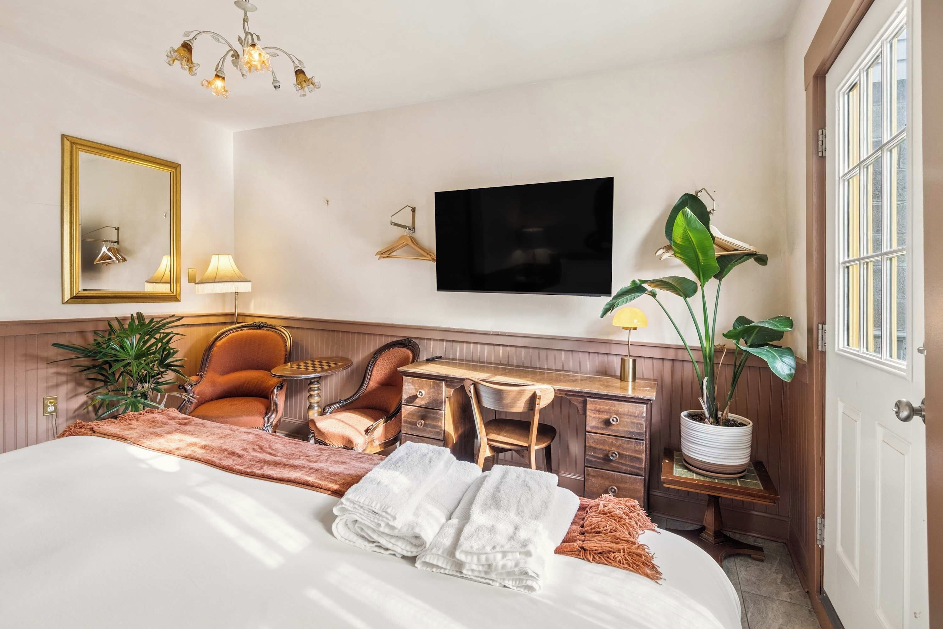 Une chambre d’hôtel équipée d’un lit, d’un bureau, d’une chaise, d’une télévision, d’un miroir et d’une plante en pot.