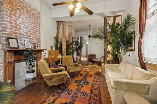 Un salon avec un mur en briques, un ventilateur de plafond, un tapis à motifs et un canapé beige.