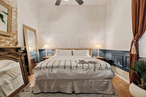 Een slaapkamer met een bed, twee nachtkastjes, een spiegel, een plafondventilator en een pot met een plant.