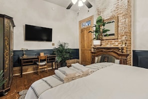Una habitación de hotel con una cama, un escritorio con una silla, un televisor, una planta y una chimenea.