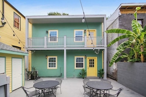 Un bâtiment à deux étages, avec une façade verte, une porte jaune et un balcon doté de balustrades. On peut voir deux tables avec des chaises au premier plan.